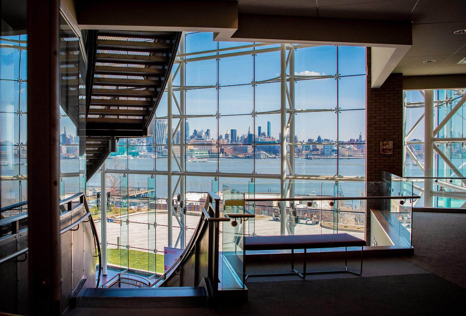 The Babbio Center atrium: a steel staircase and a glass wall looking across the Hudson River to Manhattan