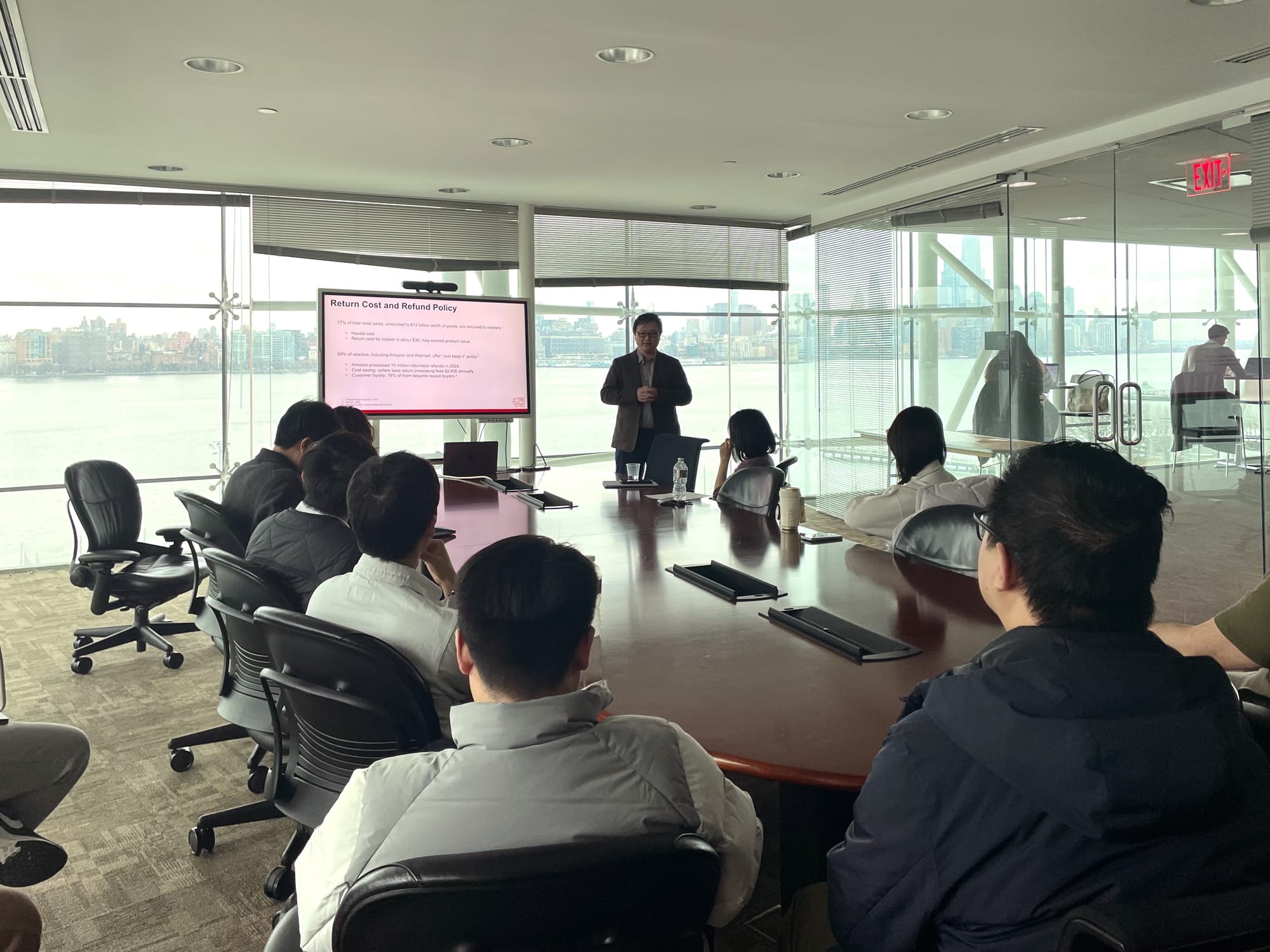 Jinan Lin presents at the end of a long conference table while the audience follows his slides