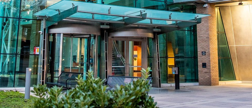 The entrance of Babbio Center under its glass canopy, seen from the plaza, with a revolving door at left and a pair of swing doors at right