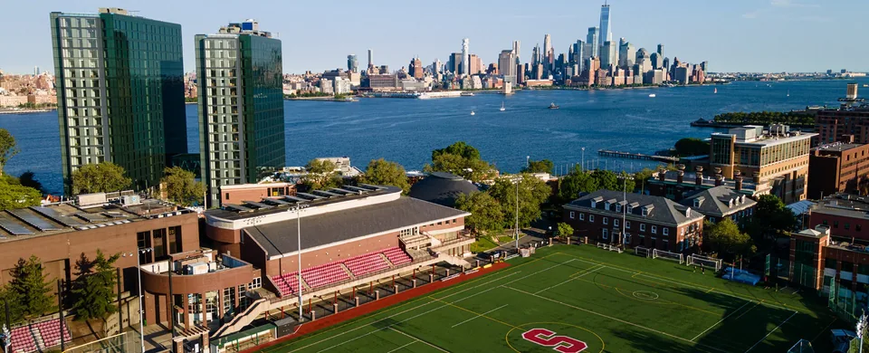Stevens campus from above: the athletic field and stands, campus buildings, the Hudson and the Manhattan skyline