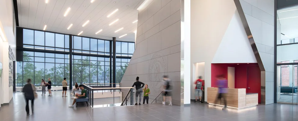 Campus commons with a window wall onto trees and the river, a stone wall carved with the Stevens seal, and a red service counter