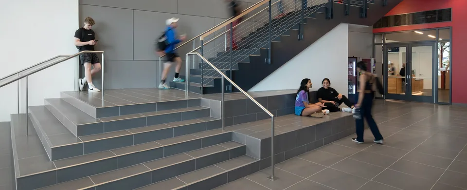 Campus staircase with tiled seating steps, steel handrails, a red wall and glass doors