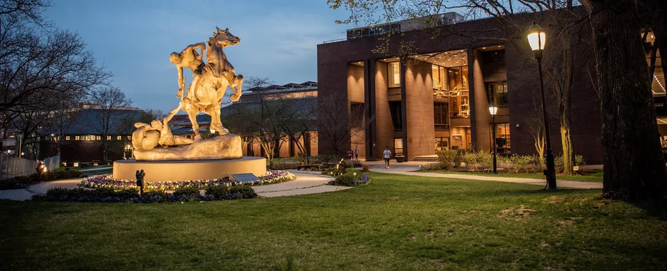 The Torch Bearer statue on a campus lawn at dusk, with a lit brick building behind