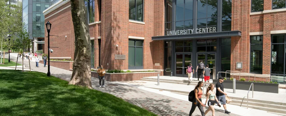 University Center entrance on a spring day, with a glass tower and the campus walk behind